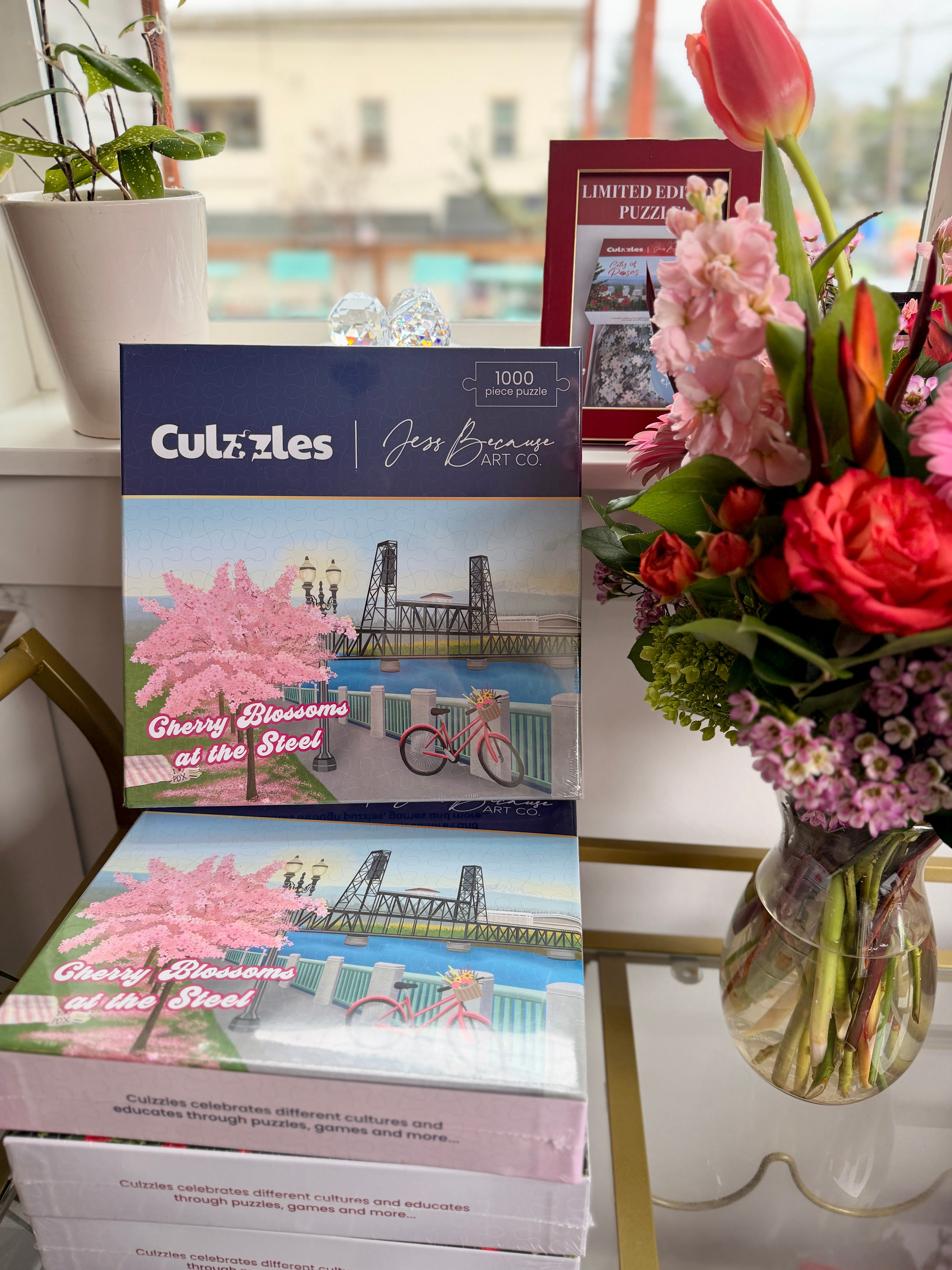 Culzzles puzzle box with cherry blossoms and a bridge design, next to a vase of flowers on a table.