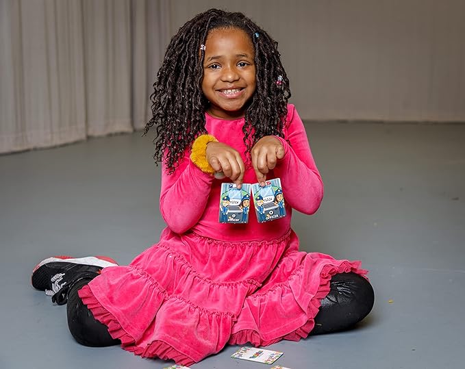 Child in a pink dress sitting on the floor holding two packages.
