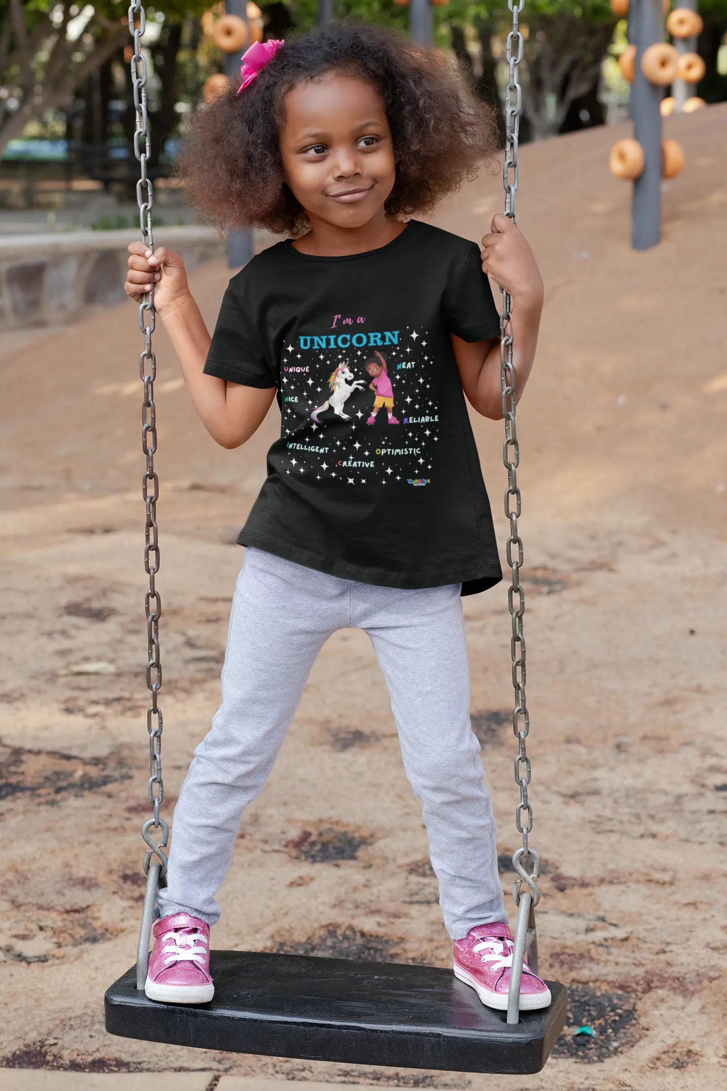 A child wearing a black culzzles unicorn t-shirt with a unicorn design on a swing at a playground.