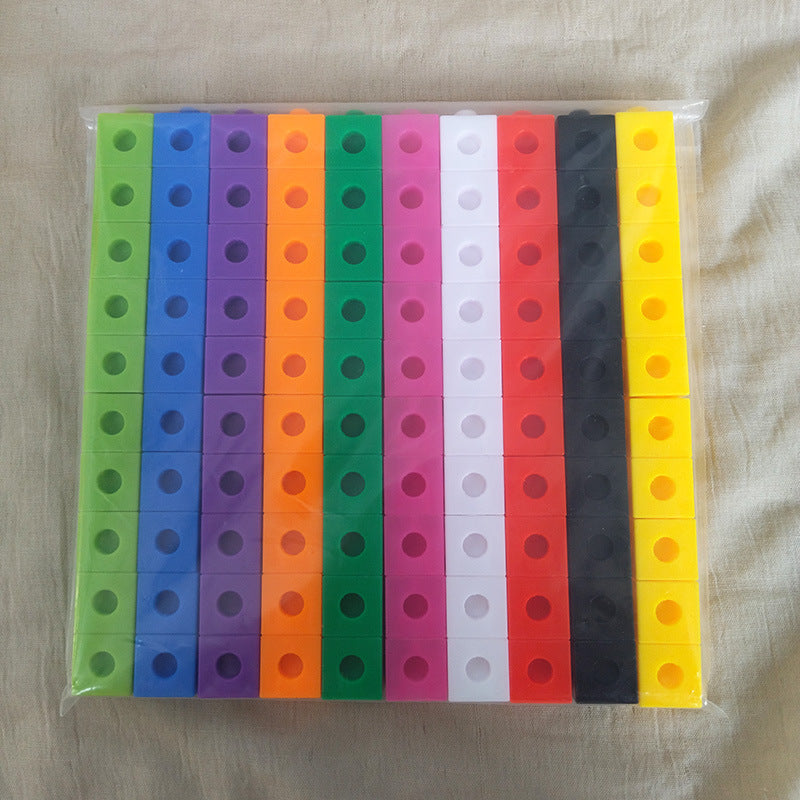 A clear plastic bag containing multiple vertical strips of colorful rectangular pieces, each with a circular hole near the top, arranged in columns of green, blue, purple, orange, green, pink, red, white, black, and yellow on a beige fabric background.